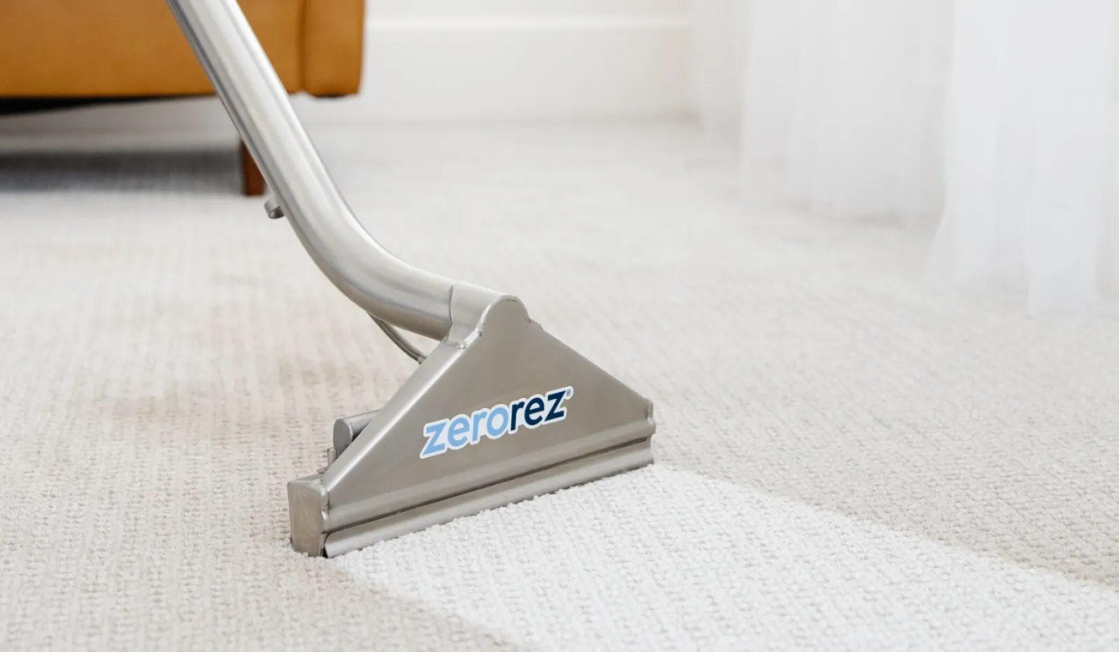 A Zerorez carpet cleaning tool in action on a light carpet in a cozy living room.