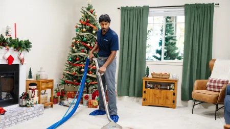 Professional cleaner using an extractor machine to clean a stained carpet in a decorated living room with Christmas tree.