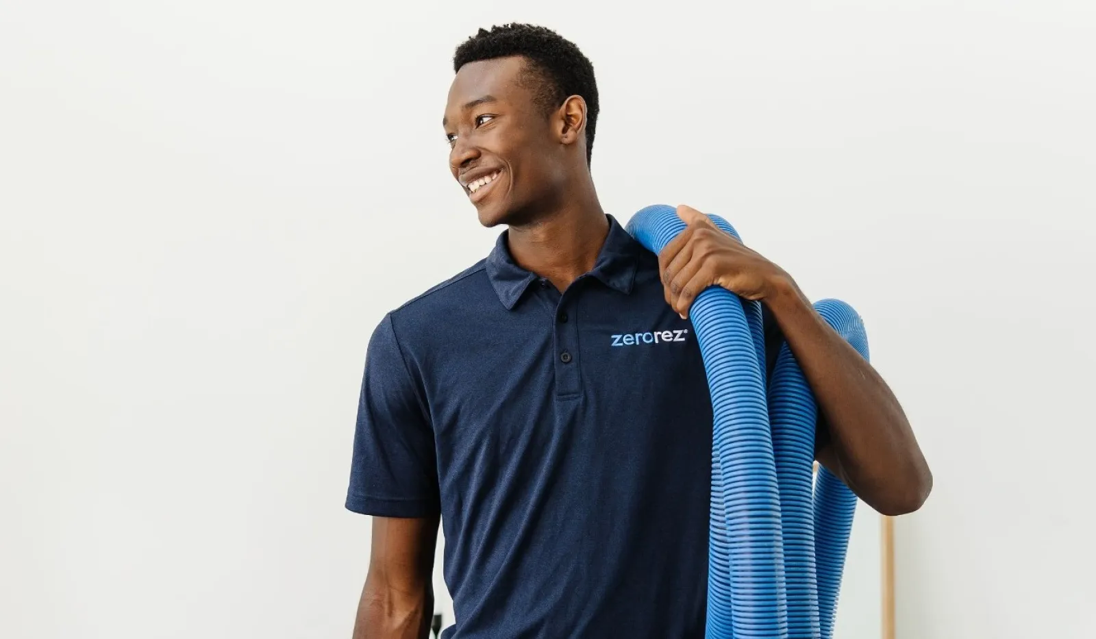 Smiling man in dark blue Zerorez shirt holding blue cleaning hose over shoulder in bright room