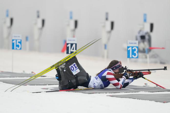A female athlete in a sit-ski is aiming with a rifle, she is lying down in the shooting range