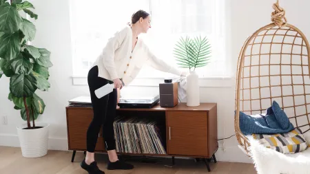 A woman cleaning a modern living room with indoor plants and vinyl records on display.