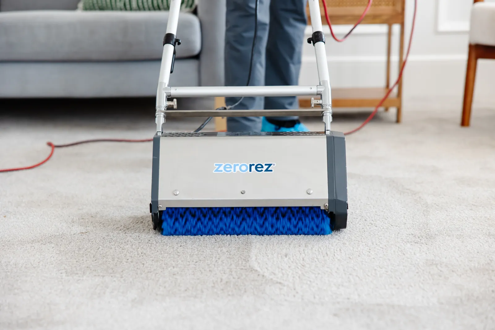 Close up of the counter rotating brushes of a Zr&trade; Lifter from Zerorez<sup>&reg;</sup> being used on a white carpet, making its fibers fluffy and kicking up all the embedded hair and dirt deep in the carpet's fibers