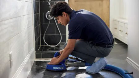 Technician cleaning black tiled floor in a bathroom using Zerorez cleaning machine and hose.