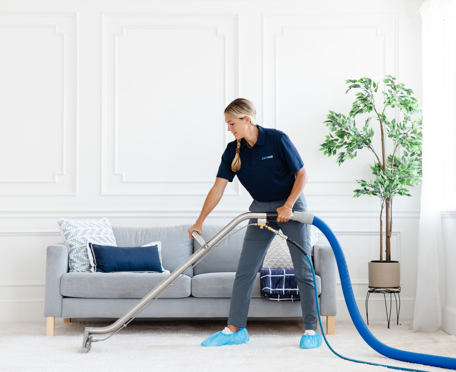 Female Zerorez&reg; technician pulling a Zr&reg; Wand to clean a white carpet with the right temperature water to clean carpets in a living room setting with a couch and tree